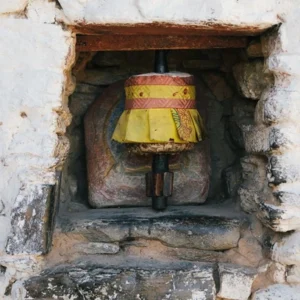 A small Bhutanese prayer wheel set inside a stone wall niche, painted in yellow and red.