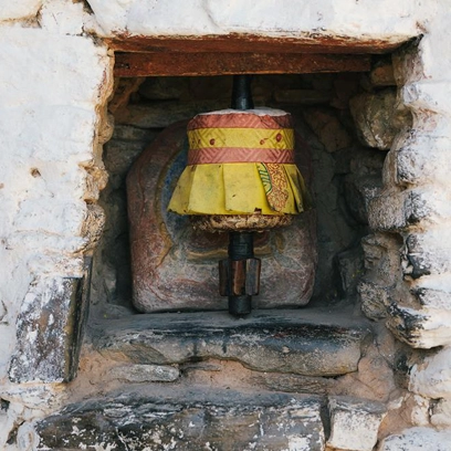 A small Bhutanese prayer wheel set inside a stone wall niche, painted in yellow and red.