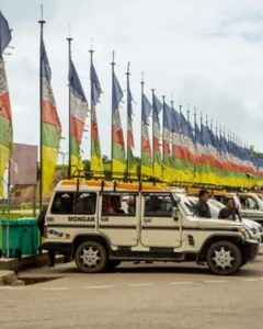 White four-wheel-drive Mongar taxi parked beside rows of colourful Bhutanese prayer flags.